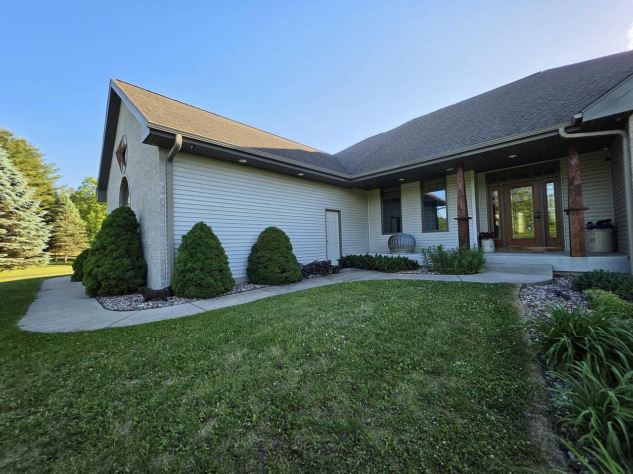 Front porch entry of 1825 Bringold Drive, with cedar timber posts, a glass front door framed by sidelights, and clipped landscape shrubs along the foundation