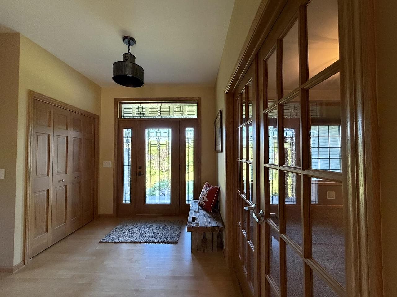 Foyer of 1825 Bringold Drive looking out the leaded-glass front door, with a closet on the left, a paneled bench on the right, and a wall of French doors with glass mullions opening into the living spaces
