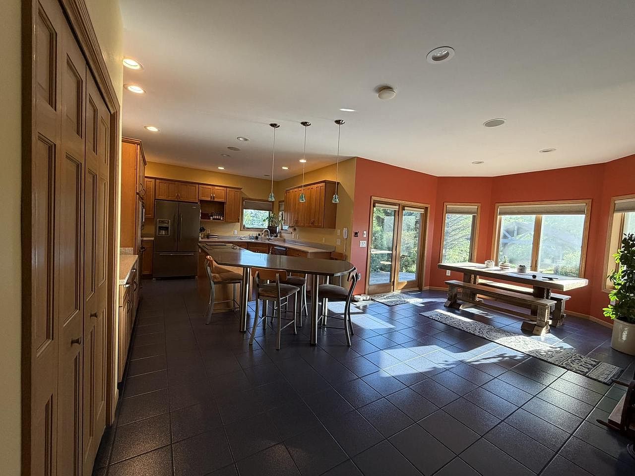 Open kitchen and dining area at 1825 Bringold Drive, with a long oval island, stainless steel appliances, recessed lighting, and the dining bay with terracotta walls and a heavy reclaimed wood farm table