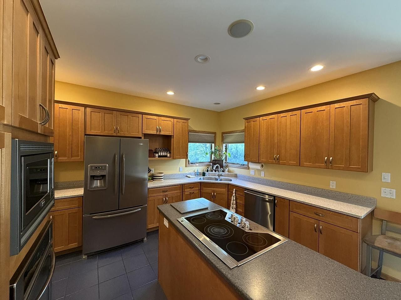 Kitchen interior at 1825 Bringold Drive with maple cabinetry, double wall oven, stainless French-door refrigerator, an electric cooktop set into the island, and corner windows letting in light over the sink
