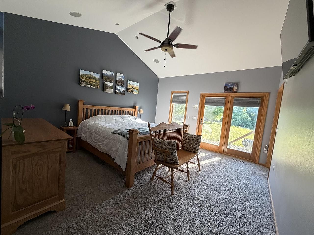 Primary bedroom at 1825 Bringold Drive with a vaulted ceiling, a slate-blue accent wall behind a mission-style bed, sliding glass doors opening onto a private deck on the right, and a grid of small framed landscape prints above the headboard